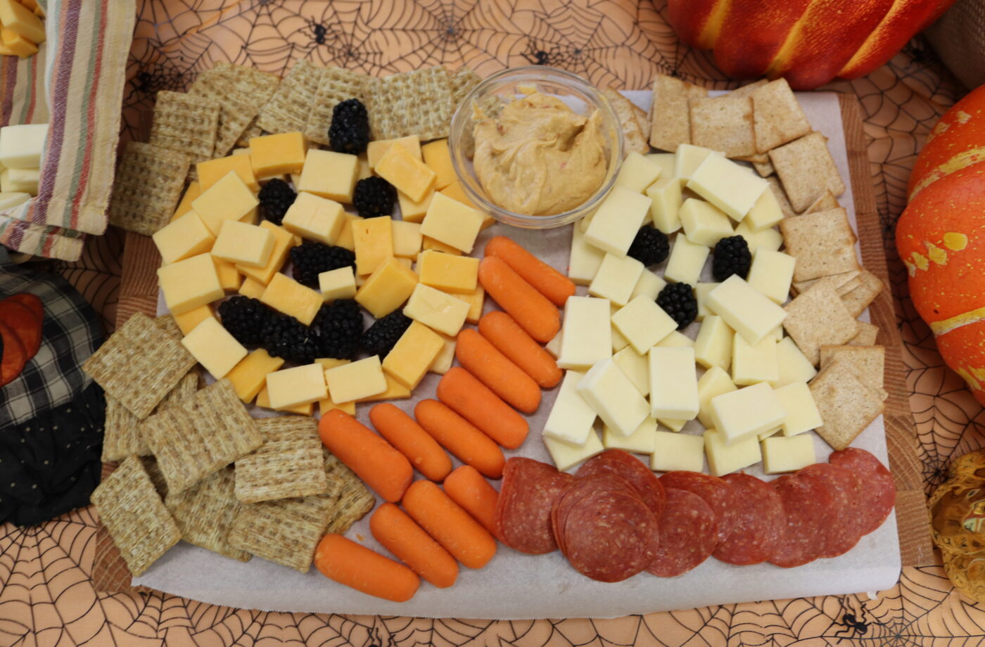 A charcuterie and cheese board photographed from above where the cheese is assembled to create a pumpkin and a ghost shape. Image accompanies easy snack recipes.